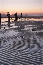 View of sand ripples and eroded groynes on the beach during low tide at sunset
