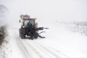 Tractor driving on a country road during a heavy snowstorm