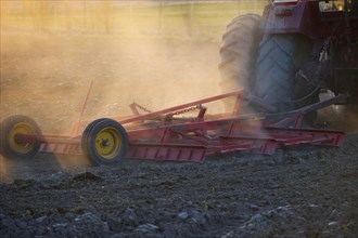 Close-up of Vaderstad cultivator cultivating a field planting bed in a dusty field at sunset