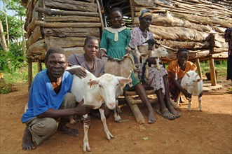 Family keeping domestic goats sitting in front of a wooden hut