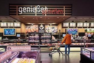 Man in orange jacket and shopping trolley standing in front of the service counter for cheese