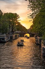 Boats sail through the canals of Amsterdam at golden hour