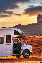 Motorhome with company logo parked on gravel road in front of striking rock formation