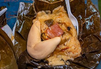 Nacatamal served with bread in a banana leaf on the table. Traditional Nacatamal served in banana leaf