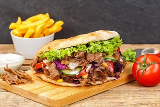 Doener Kebab Doner Kebap fast food meal in pita bread menu with fries on wooden board in Stuttgart