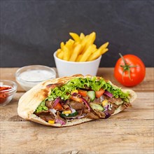 Doener Kebab Doner Kebap fast food meal in pita bread menu with fries on wooden board square in Stuttgart