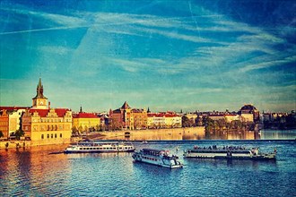 Vintage retro hipster style travel image of Vltava river with tourist boats and Prague Stare Mesto embankment view from Charles bridge on sunset with grunge texture overlaid. Prague