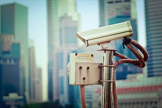 Vintage retro hipster style travel image of CCTV surveillance camera in Singapore with skyscapers in background
