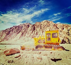 Vintage retro effect filtered hipster style travel image of Bulldozer doing road construction in Himalayas. Ladakh