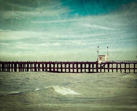 Vintage retro hipster style travel image of pier in ocean with grunge texture overlaid