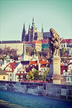 Vintage retro hipster style travel image of statue on Charles Brigde with St. Vitus Cathedral in background in Prague