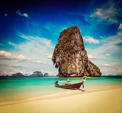 Vintage retro effect filtered hipster style travel image of long tail boat on tropical beach with limestone rock