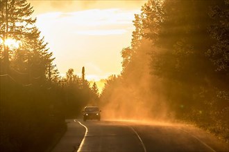 A car is driving on a road covered with a colorful fog at sunset