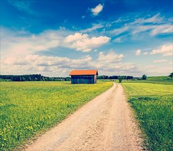 Vintage retro effect filtered hipster style image of rural road in summer meadow with wooden shed. Bavaria
