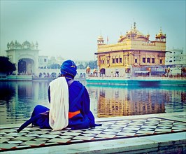 Vintage retro hipster style travel image of unidentifiable Seekh Nihang warrior meditating at Sikh temple Harmandir Sahib. Amritsar