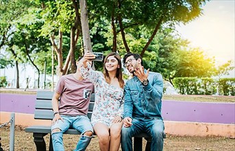 Three friends sitting on a bench taking a selfie