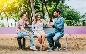 Three happy friends talking in a park. Three teenage friends talking sitting on a park bench