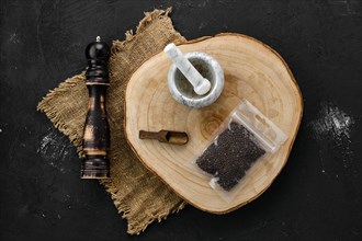 Wooden cross section with peppercorn in plastic package and stone mortar and mill