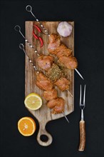 Top view of skewers with raw turkey meat with sweet and spicy rub on dark background