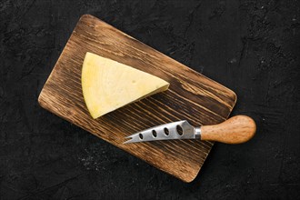 Top view of triangular piece of hard cheese on wooden cutting board