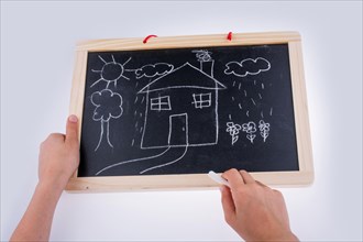 Hand drawing a house on the blackboard with a chalk