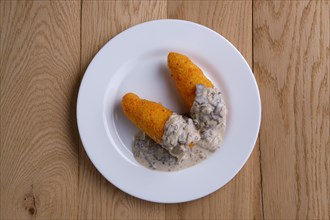 Top view of potato cutlet in breading stuffed with ham served with mushroom sauce on wooden table