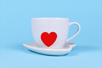 White tea cup with red heart shaped tea bag paper on blue background