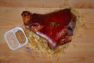 Top view of knuckle with sauerkraut served with mustard and horseradish on wooden cutting board