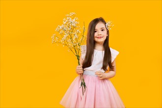 Cute young girl with wildflowers bouquet in hands on yellow background