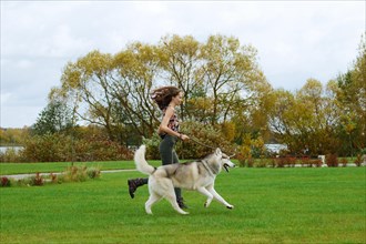 Girl playing with husky dog in city park. Jogging with dog