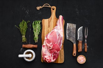 Fresh raw lamb leg bone in on wooden cutting board with herbs and seasoning