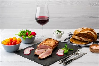 Sliced grilled pork fillet with fresh tomatoes and raddish served with glass of red wine