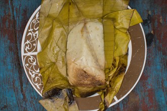 Traditional Tamal Pisque stuffed in banana leaf served on wooden table