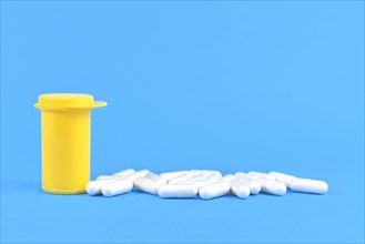 Capsule pills next to yellow medicine container on bright blue background