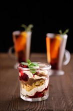 Delicious tiramisu dessert with cherry and citrus tea on dark wooden background