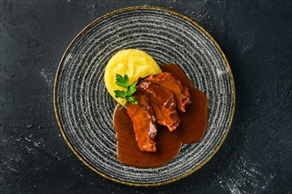 Overhead view of roasted beef slices with wine sauce and mashed potato on dark background