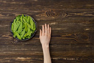 Overhead view of fresh green peas in a pods in hand over wooden background