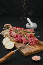 Sprinkling with spice rub raw beef meat on skewer on dark background