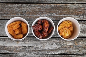 Top view of three cardboard containers with fried chicken wings on wooden table