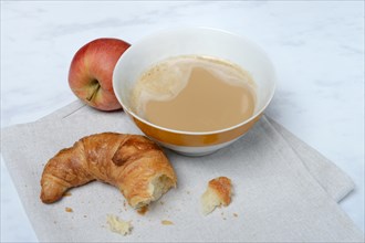 Coffee with milk in bowl and croissant