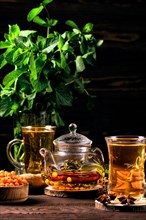 Low key photo of hot herbal tea with sea buckthorn and mint on wooden table
