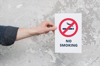 Male hand holding paper with no smoking sign text weathered wall