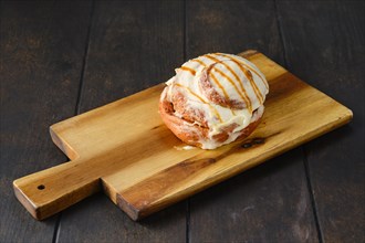 Cinnabon bun with caramel and icing on wooden serving board