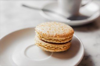 Close up photo of macaron with salted caramel on a white saucer with blurred cup of coffee on the background
