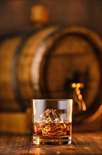 Glass of whisky with ice with barrel on background