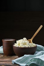 Cottage cheese with wooden spoon in it and milk in clayware on wooden table