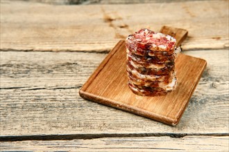 Close up view of smoked dried stacked slices of beef sausage on wooden cutting board