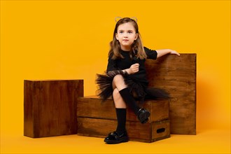Young girl sitting among wooden apple boxes on orange background