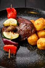 Closeup view of grilled beef with vegetables and potato balls on a plate