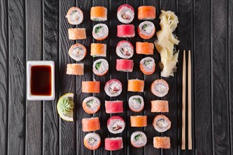 Large set of rolls with garnish and hashi on dark wooden plate
